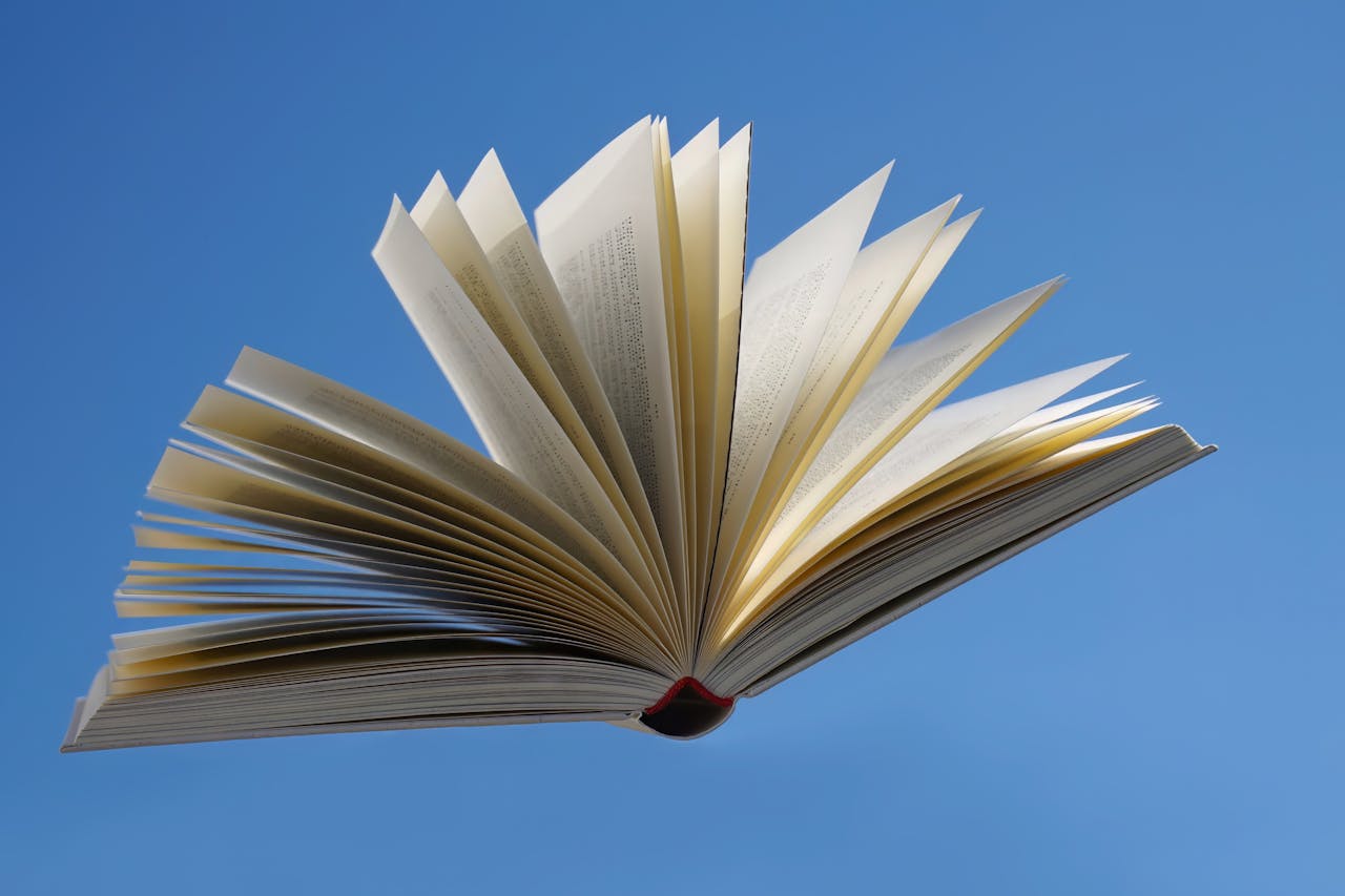 An open book with pages fanned out, floating against a bright blue sky, symbolizing imagination and knowledge.