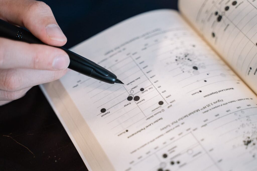 Close-up view of a hand holding a pen pointing at data in an open textbook.