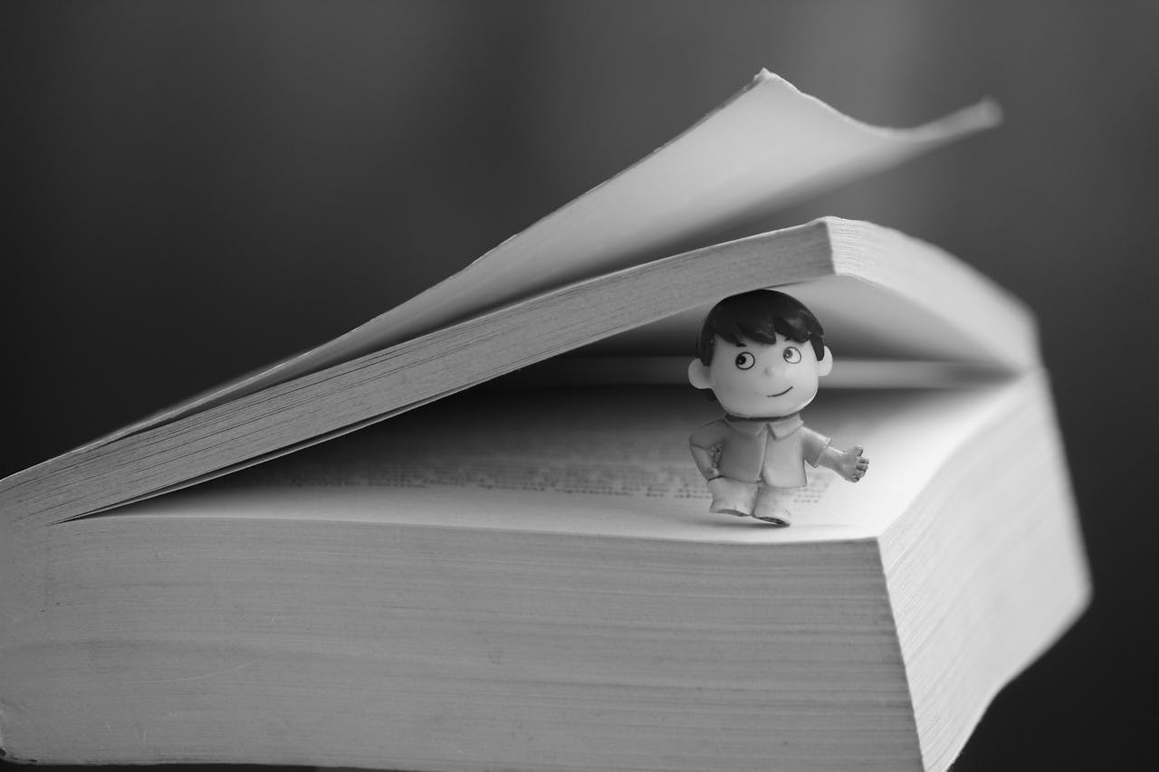A monochrome image of a tiny figure peeking from between book pages, conveying curiosity and imagination.